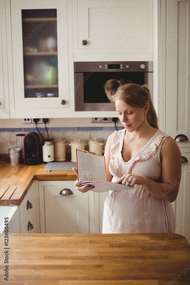 Pregnant woman reading book in kitchen Pregnant woman reading book in kitchen