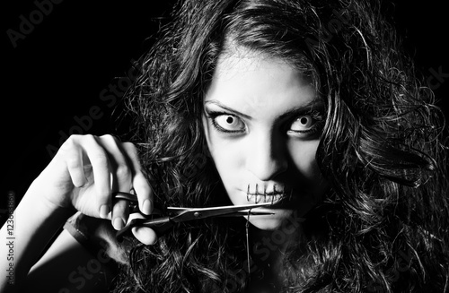 Horror shot: scary strange girl with mouth sewn shut cutting off the thread
