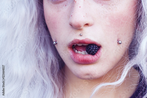 Primer plano de la boca de una chica joven con piercings comiendo una mora  photo