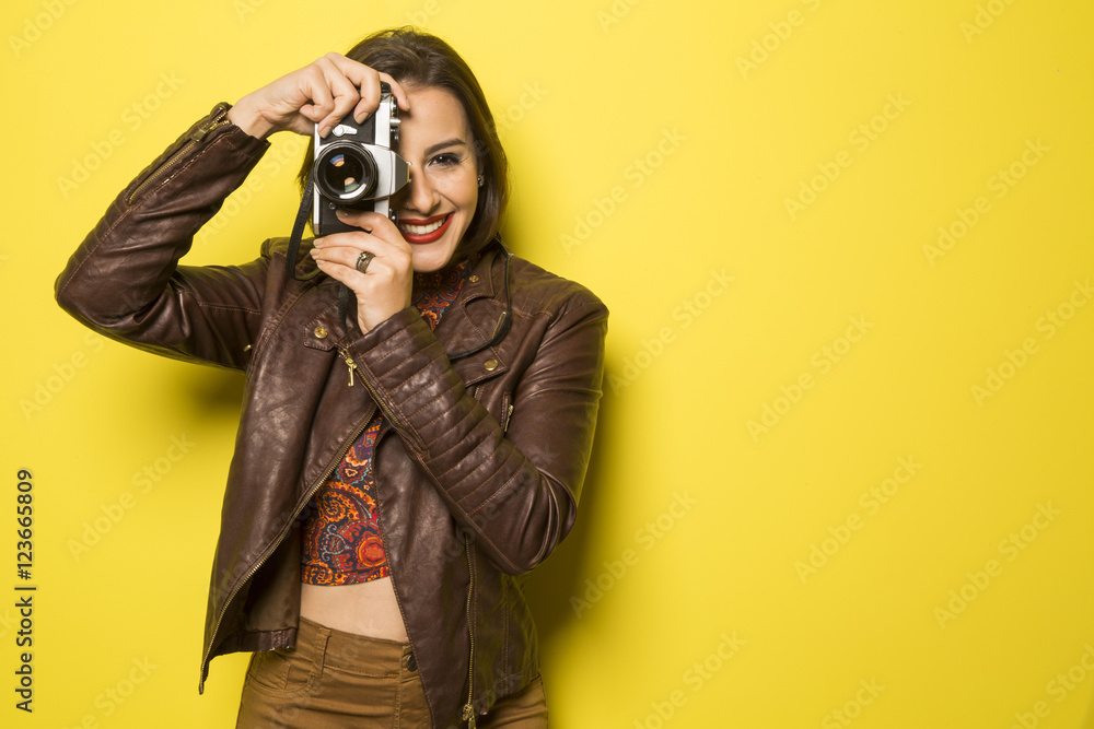 Fashion young girl makes the photo with old camera. Yellow backg Fashion young girl makes the photo with old camera. Yellow backg