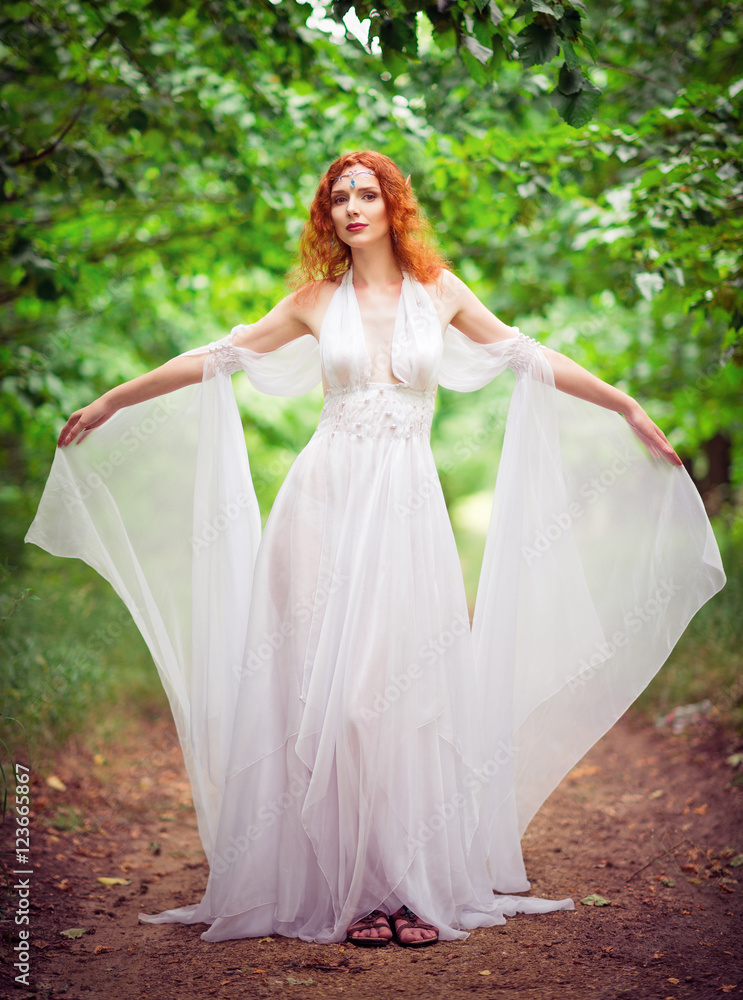 Beautiful redhead elf woman wearing white dress in a garden