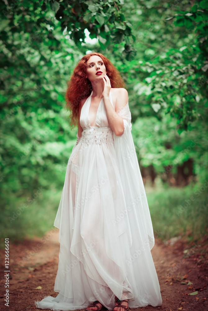 Beautiful redhead woman wearing white dress, in a forest