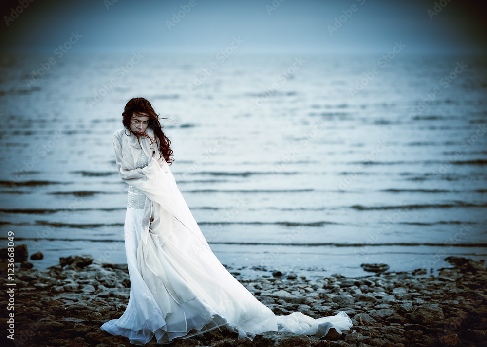 Beautiful sad girl in white dress standing on sea coast Stock Photo | Adobe  Stock
