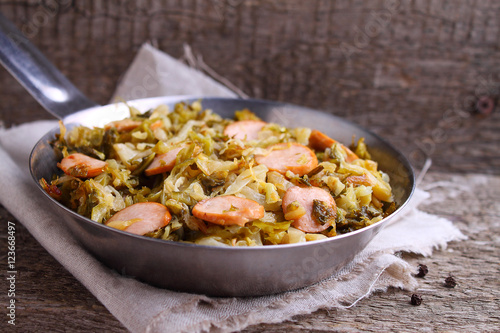 Cabbage stew with sausages in a frying pan on a wooden background
