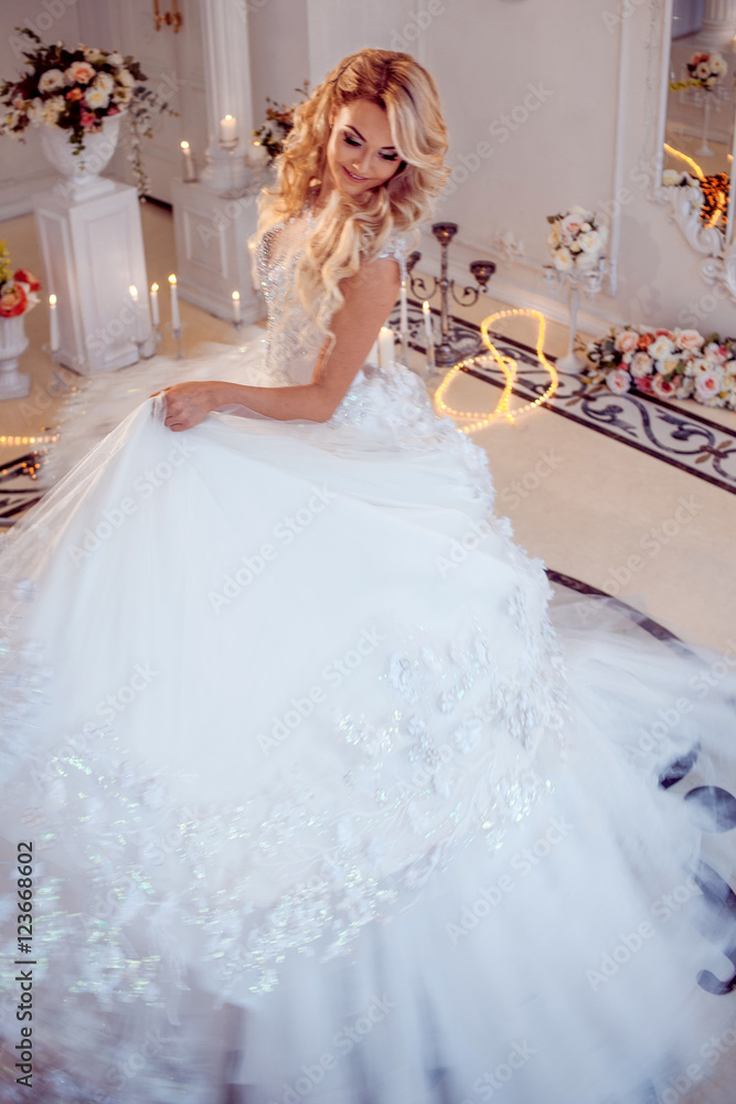 Young beautiful bride in luxurious wedding dress. Huge puffy skirt with train. Luxury light interior Young beautiful bride in luxurious wedding dress. Huge puffy skirt with train. Luxury light interior