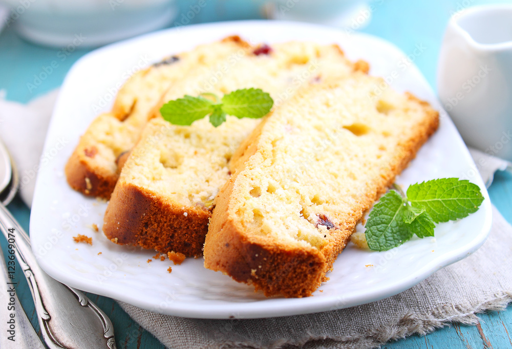 a piece of cake with raisins and candied fruit on a white plate on a blue background