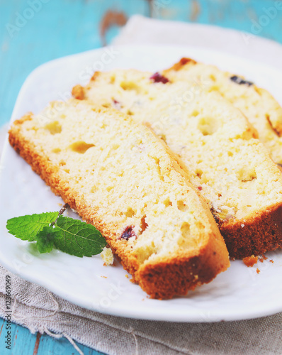 a piece of cake with raisins and candied fruit on a white plate on a blue background