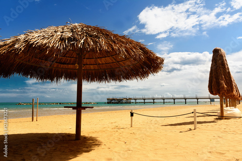 Palm umbrellas on the beach and pier in background in Francavill