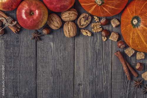 Wooden background with pumpkin, apples, nuts and spices.