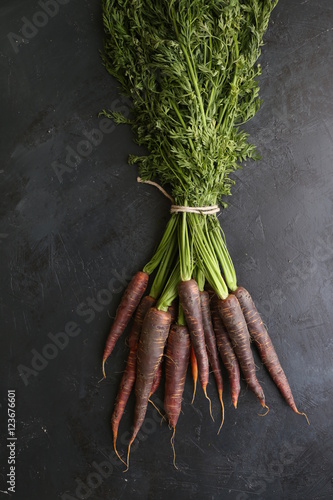 Ripe black carrots. Dark stone background. Autumn harvest.