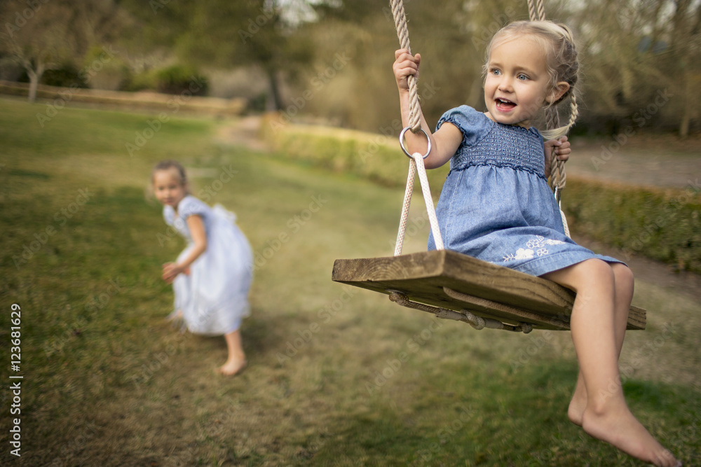 Two happy sisters playing on a swing in the garden. Two happy sisters playing on a swing in the garden.