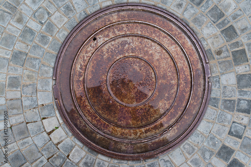 Closeup photo of Old Sewer rust manhole cover on the urban asphalt road. Rain scene.