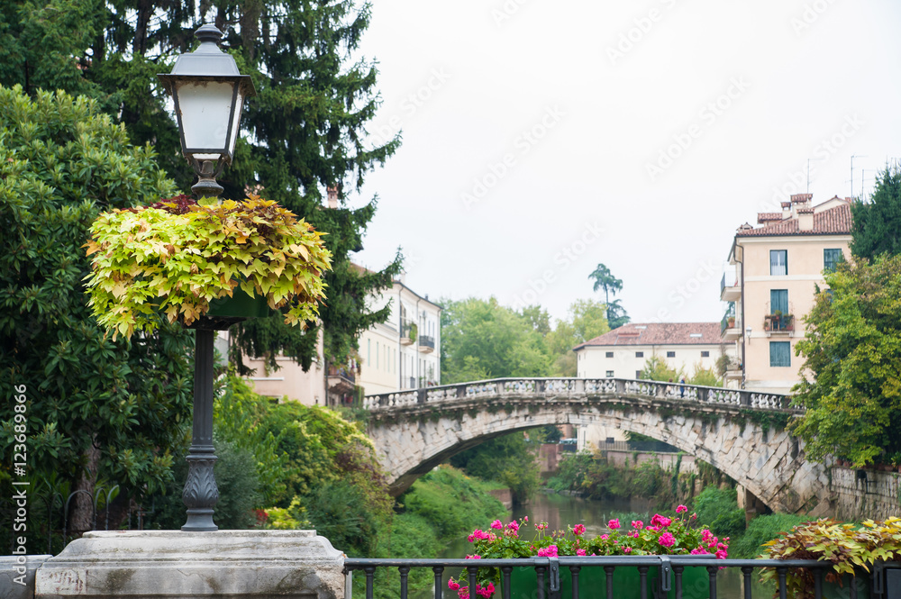 Flowered street lamp along Saint Paul bridge in Vicenza, Saint Michele bridge in the background