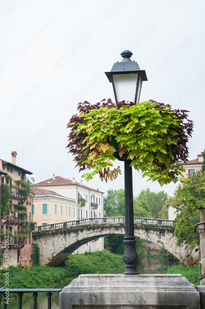 Flowered street lamp along Saint Paul bridge in Vicenza, Saint Michele bridge in the background Flowered street lamp along Saint Paul bridge in Vicenza, Saint Michele bridge in the background