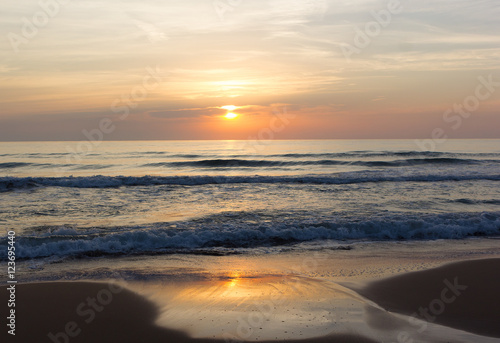 Golden wave on a sandy beach at sunrise. Ocean sunrise on a quiet morning.