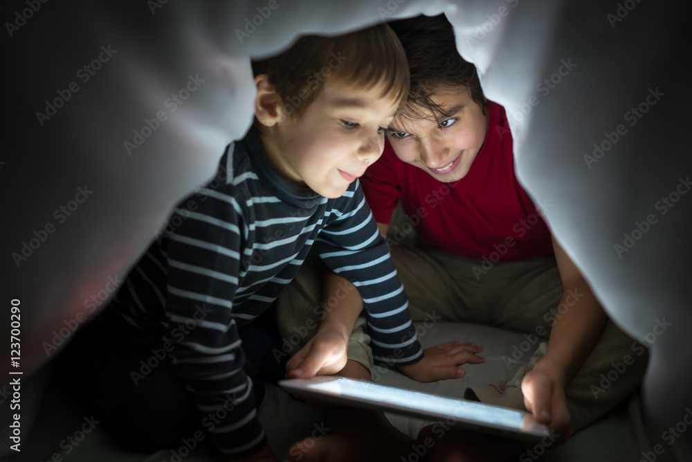 Brothers kids with tablet computer under blanket at night in a d Brothers kids with tablet computer under blanket at night in a d