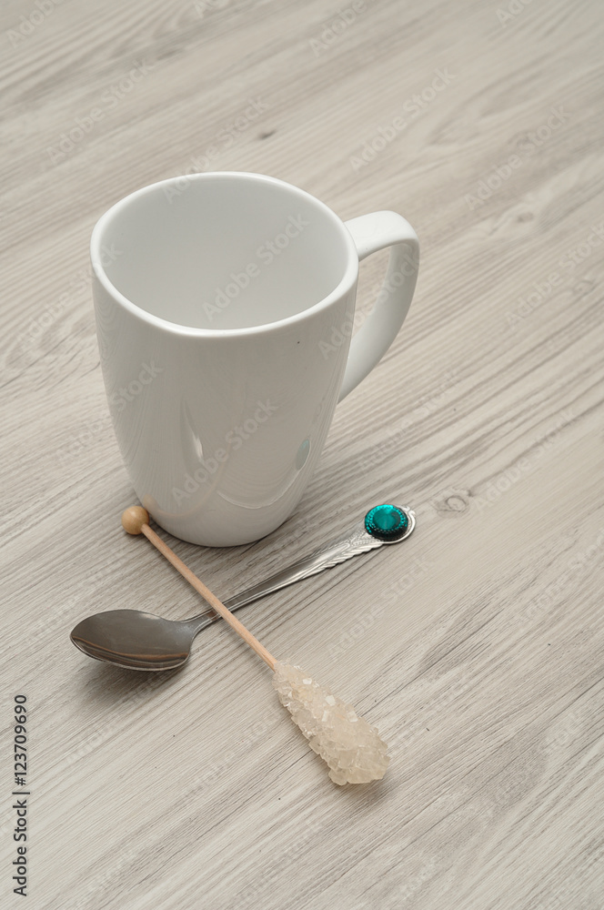 A white mug with a sugar stick and a teaspoon A white mug with a sugar stick and a teaspoon