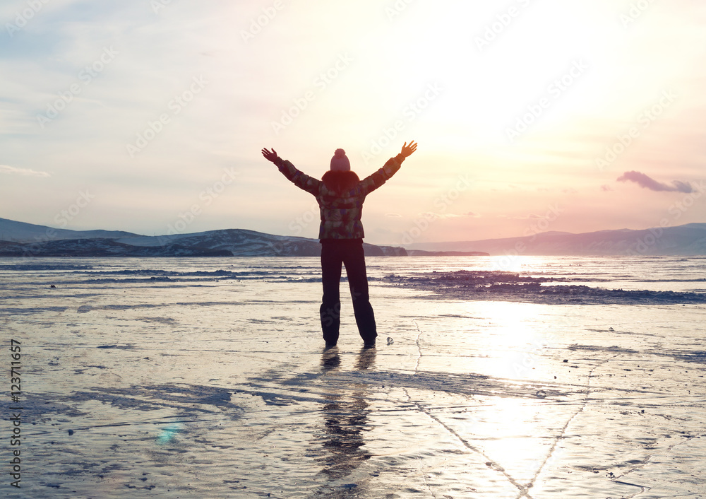 Fototapeta premium Silhouette of woman sitting at frozen lake Baikal surface enjoying sunset. Winter tourism concept