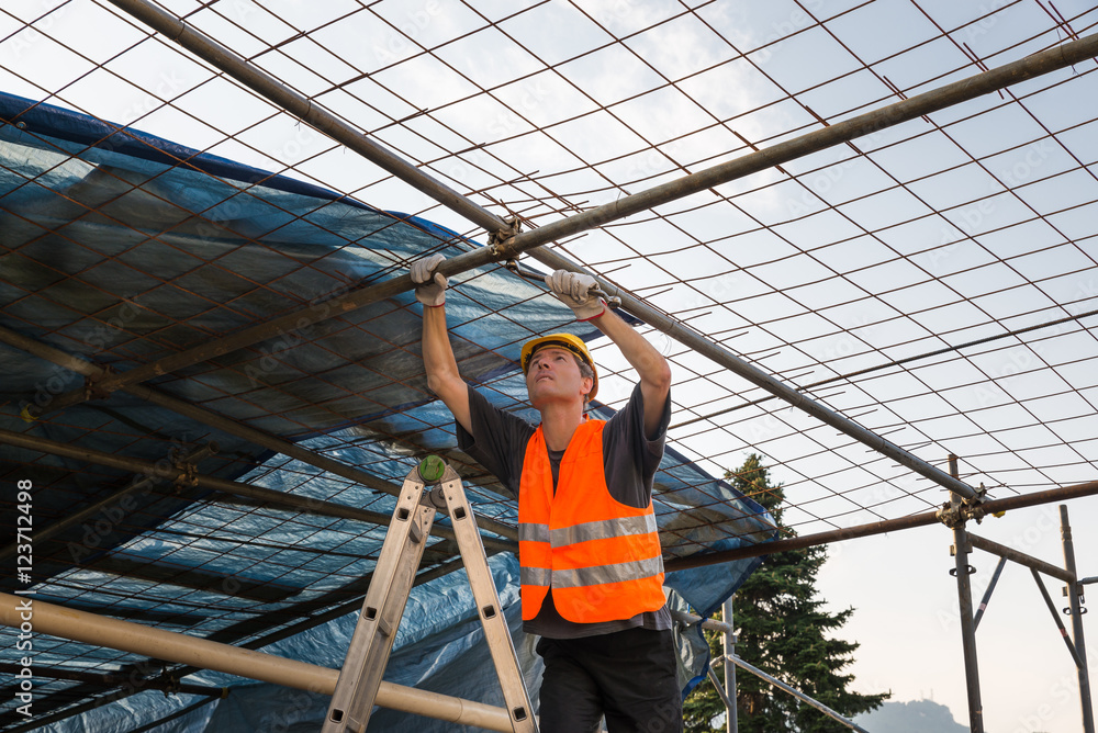 Construction worker, with helmet and reflective jacket, putting up scaffolding  