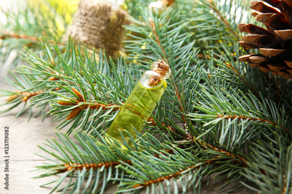 Bottle of coniferous essential oil and branches on wooden background, close up view Bottle of coniferous essential oil and branches on wooden background, close up view