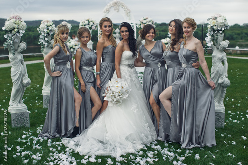 The smiling bridesmaids and bride stand near statuette with flow photo