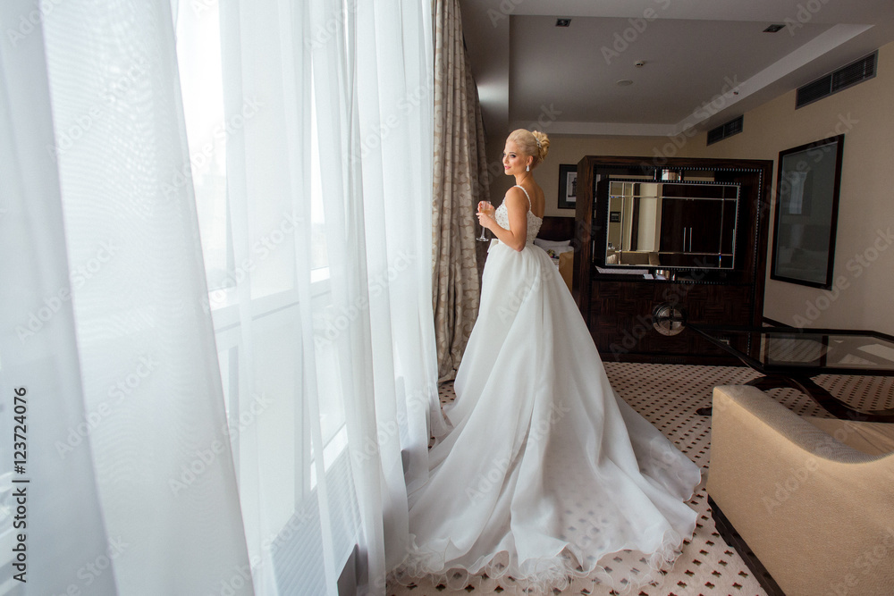 Stunning bride stands with a glass of champagne behind a window Stunning bride stands with a glass of champagne behind a window