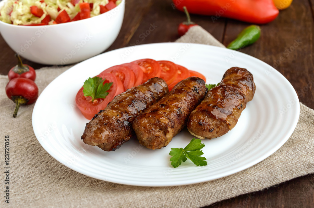 Juicy grilled rolls of minced meat wrapped in bacon with fresh tomato and a light salad of Chinese cabbage and bell pepper. Juicy grilled rolls of minced meat wrapped in bacon with fresh tomato and a light salad of Chinese cabbage and bell pepper.