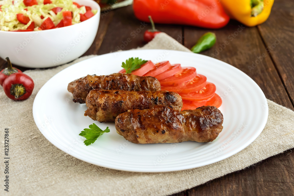 Juicy grilled rolls of minced meat wrapped in bacon with fresh tomato and a light salad of Chinese cabbage and bell pepper. Juicy grilled rolls of minced meat wrapped in bacon with fresh tomato and a light salad of Chinese cabbage and bell pepper.
