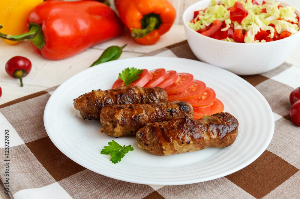 Juicy grilled rolls of minced meat wrapped in bacon with fresh tomato and a light salad of Chinese cabbage and bell pepper. Juicy grilled rolls of minced meat wrapped in bacon with fresh tomato and a light salad of Chinese cabbage and bell pepper.