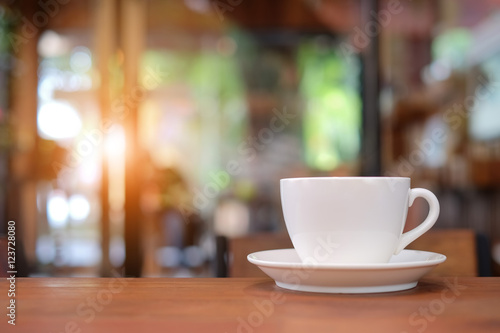 White coffee cup on wooden table with blurred cafe background.