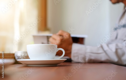 Man reading a book with white coffee cup front place.