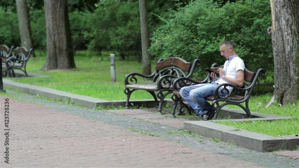 guy sitting on the bench/student sitting on a park bench with a tablet in hand guy sitting on the bench/student sitting on a park bench with a tablet in hand