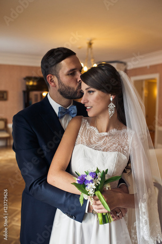 Bride looks far away in the window standing in groom's hugs insi photo