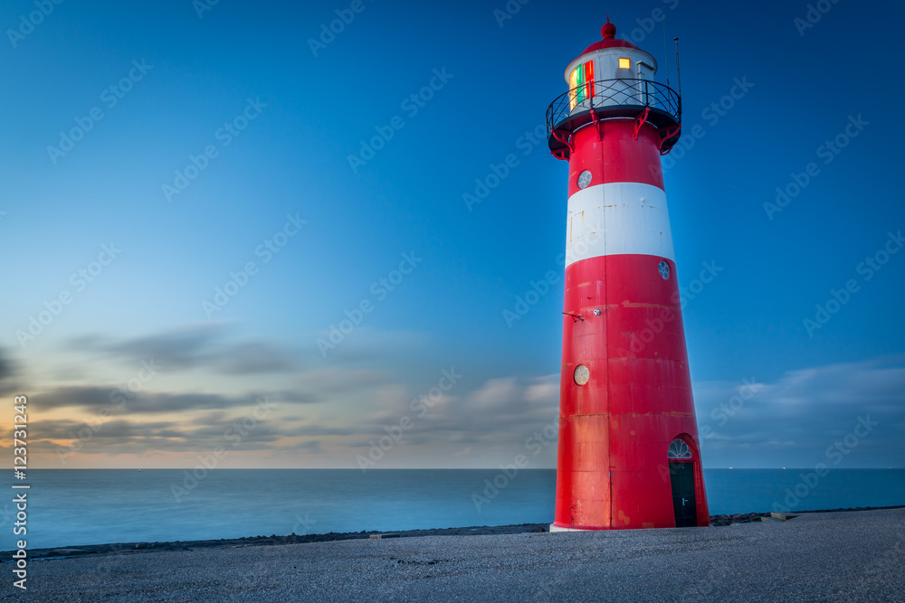 Red lighthouse during sunset on a dike at sea