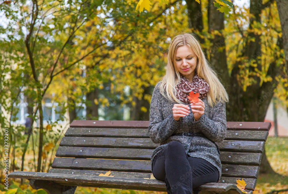 In autumn when leaves become colorful young, beautiful, gentle woman sitting and resting on the bench in the park in evening light. In autumn when leaves become colorful young, beautiful, gentle woman sitting and resting on the bench in the park in evening light.