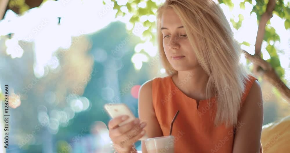 Young, attractive , girl sitting outdoors at a cafe using a smartphone Young, attractive , girl sitting outdoors at a cafe using a smartphone