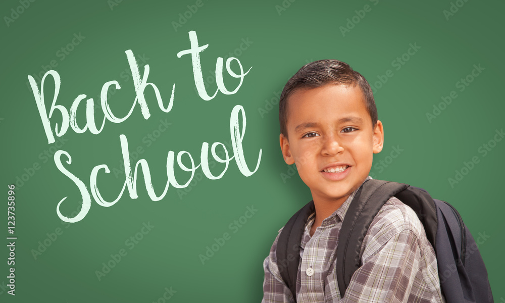 Cute Hispanic Boy Wearing A Backpack In Front of Chalk Board with Back To School Written On it. Cute Hispanic Boy Wearing A Backpack In Front of Chalk Board with Back To School Written On it.