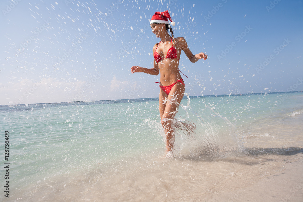 femme heureuse courant sur la plage avec un bonnet de père Noël et un  maillot de bain rouge Photos | Adobe Stock