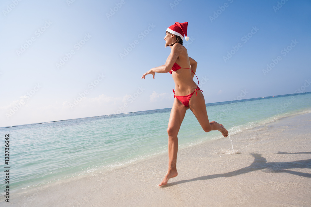 femme heureuse courant sur la plage avec un bonnet de père Noël et un  maillot de bain rouge Stock Photo | Adobe Stock