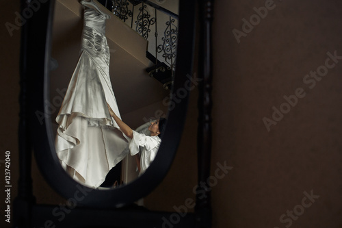 The bride stands near a wedding dress