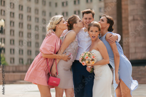 Girls are kissing a groom next to the bride in the wedding day