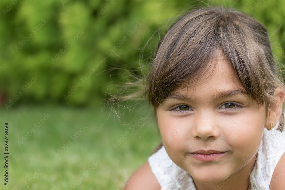 Closeup view of the slightly smiling face of little girl lying on the grass outdoors. Closeup view of the slightly smiling face of little girl lying on the grass outdoors.