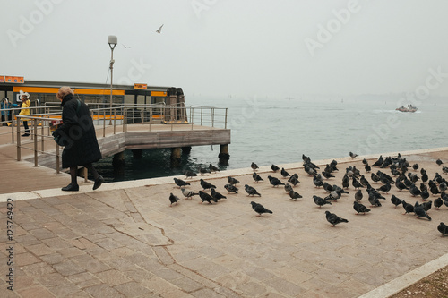 Little lady in black coat walks away from pigeon flock along the photo