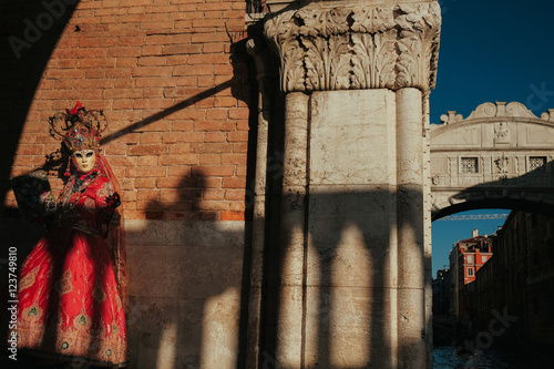 Woman in carnival dress poses leaning to the wall behind a chann photo