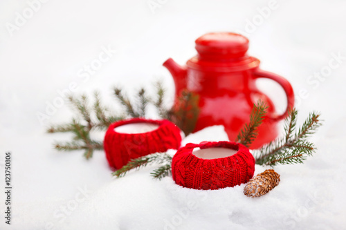 Red cups in knitted covers and a kettle in the snow. Winter picnic.