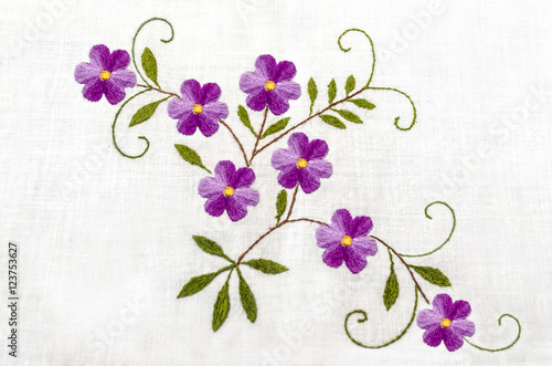 Gentle purple flowers with leaves embroidered satin stitch on white cloth