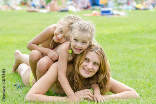 Two daughters happily sit on mom back, hot summer day relaxing on the green lawn © madhourse