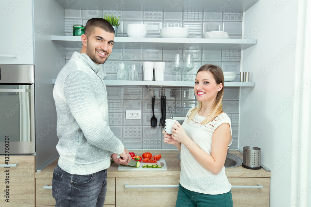 Wunschmotiv: Happy young couple is preparing food in the kitchen. Young man is slicing vegetables on
