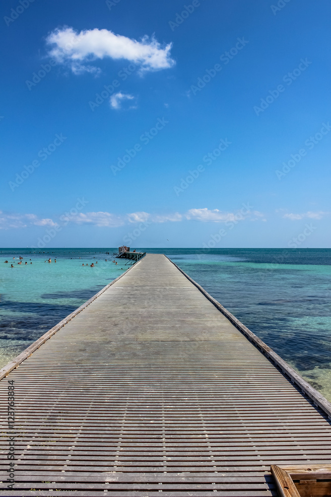 Wooden pier in Higgs Beach, a popular Key West beach in Florida known for snorkeling, tropical turquoise waters and white sand. Infinity and freedom concept.