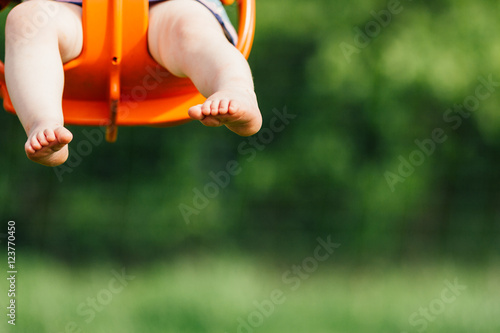 Focus on toddler girl's feet and legs as she swings in an orange baby swing at a playground